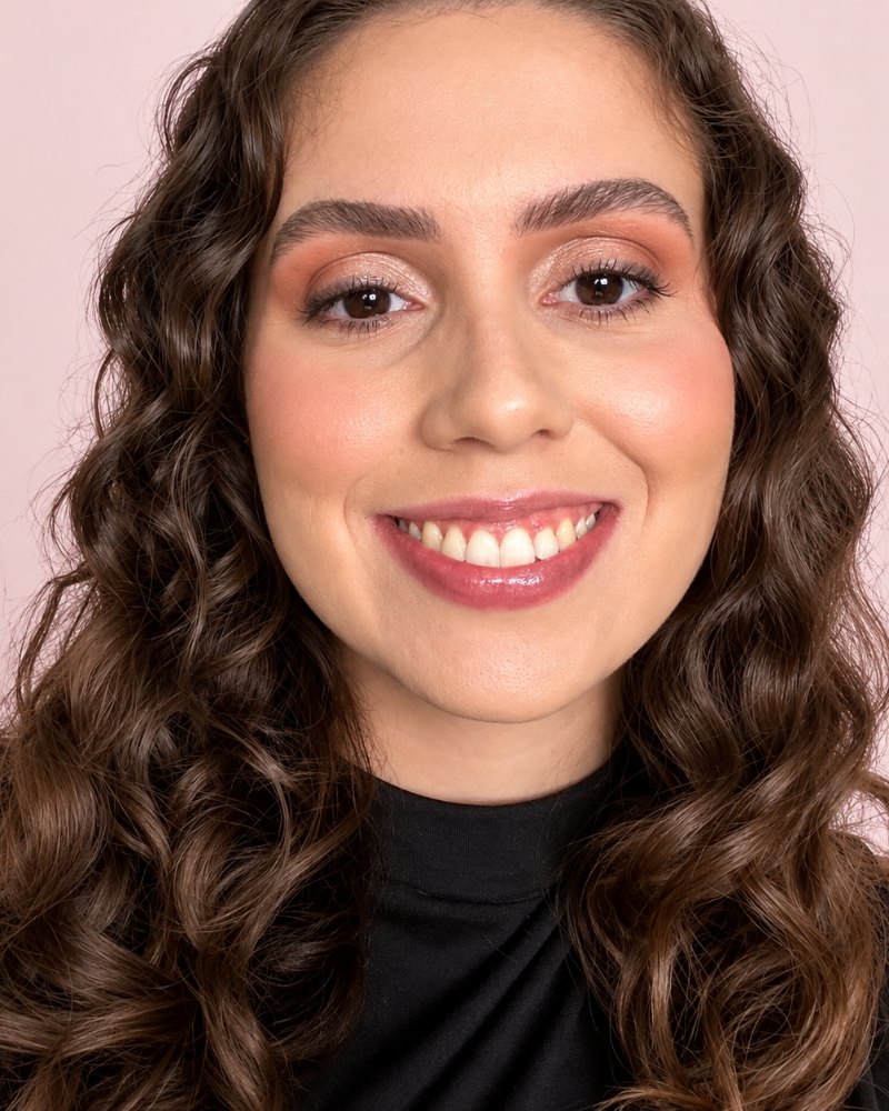 Retrato de Ana C. Alves sorrindo, de cabelos cacheados e blusa preta, sobre fundo rosa claro